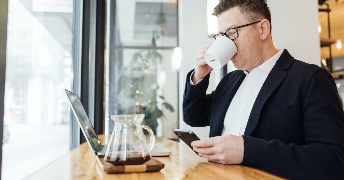 Business person drinking from mug while sitting in front of laptop and mobile phone